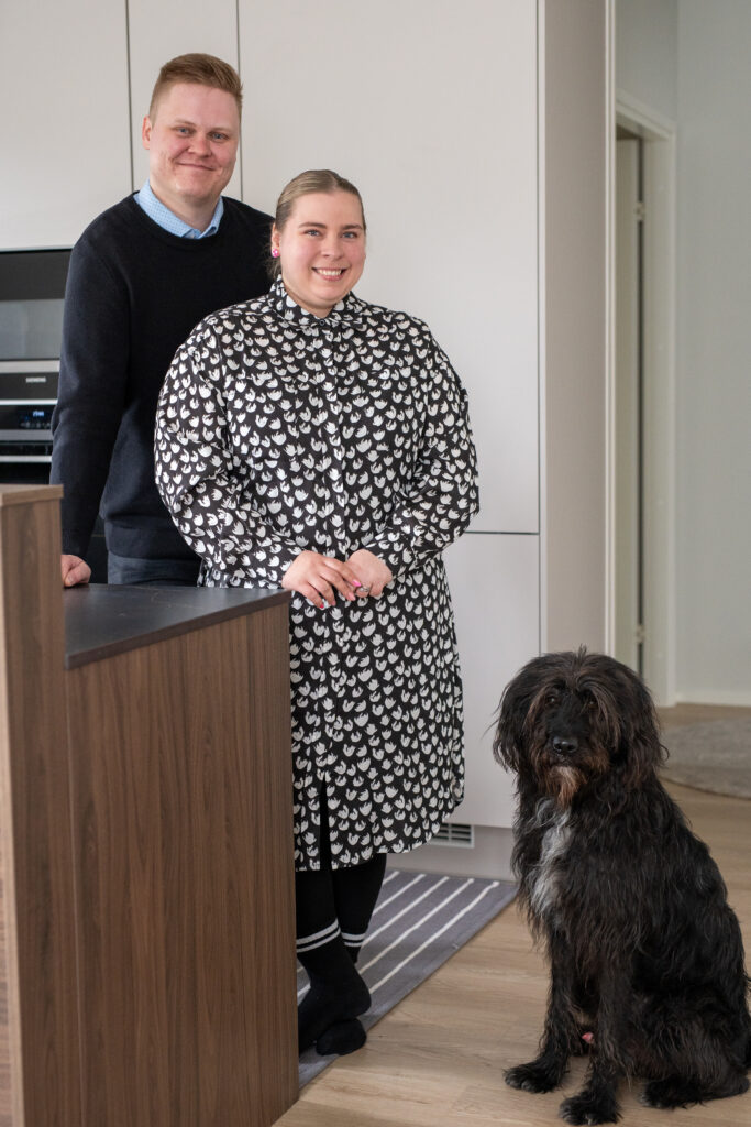 pariskunta ja koira keittiössä katsoen kameraan